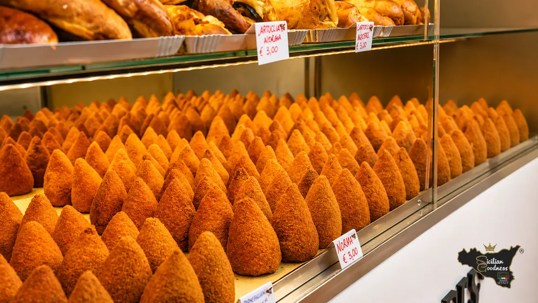 Vetrina Sicilian Goodness con arancini siciliani dorati e specialità di rosticceria